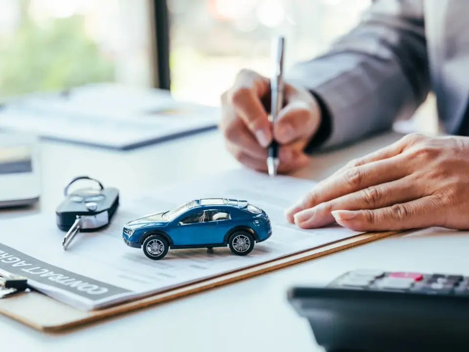 Consultor assinando um contrato ao lado de uma miniatura de carro e uma chave